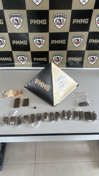 Table com materiais apreendidos, incluindo pacotes de substância vegetal, uma nota de dinheiro e uma pirâmide preta e dourada com a sigla PMMG ao fundo.