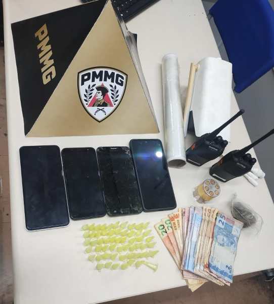 Material apreendido incluindo celulares, dinheiro, e objetos diversos em uma mesa.