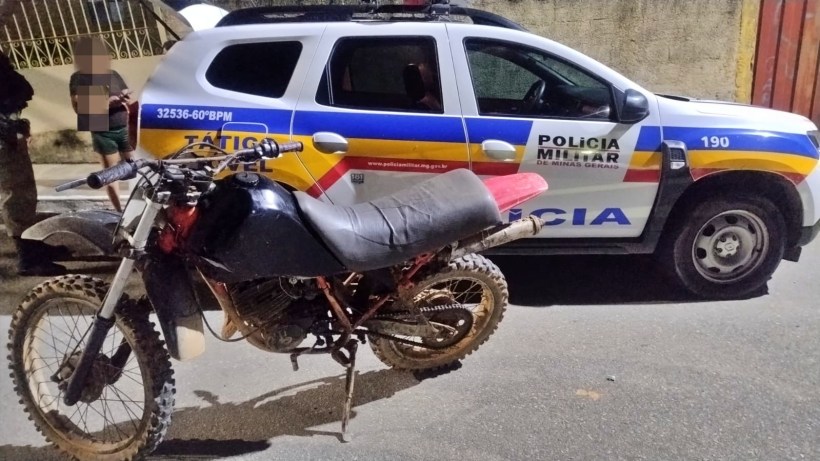 Moto off-road preta ao lado de uma viatura da Polícia Militar, com a pintura característica do Brasil.