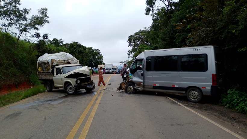 Acidente de trânsito envolvendo uma caminhonete branca e um micro-ônibus na estrada, com pessoas nas proximidades avaliando os danos.