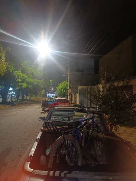 Caminho à noite com árvores ao fundo e duas bicicletas na caçamba de uma caminhonete.