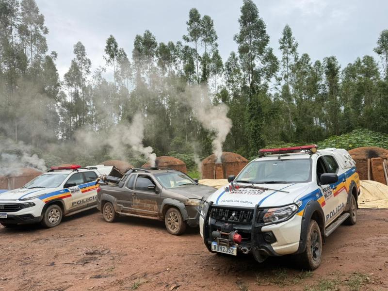 Veículos da polícia rural em uma área de floresta, com fumaça saindo de estruturas ao fundo.