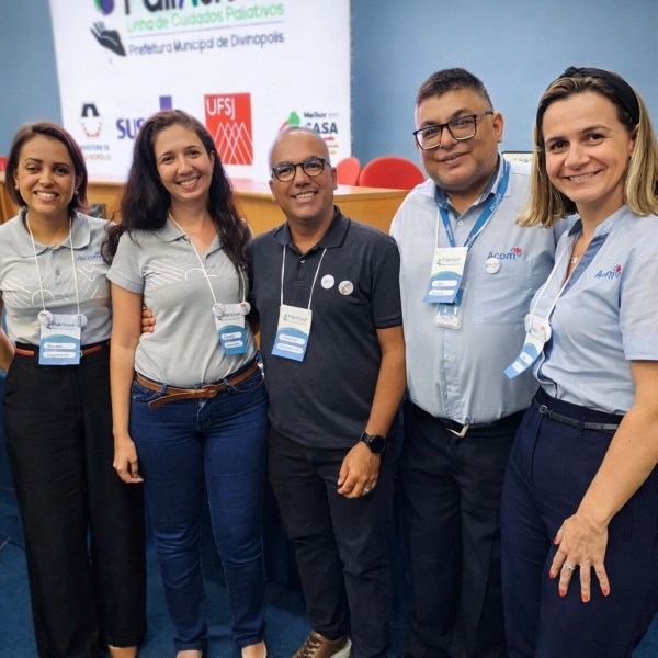 Cinco pessoas sorrindo em um evento, usando camisetas com logotipos e crachás, em um ambiente de conferência.