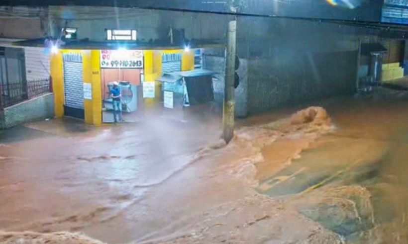 Rua inundada com água suja, com um estabelecimento comercial visível ao fundo, durante a noite.