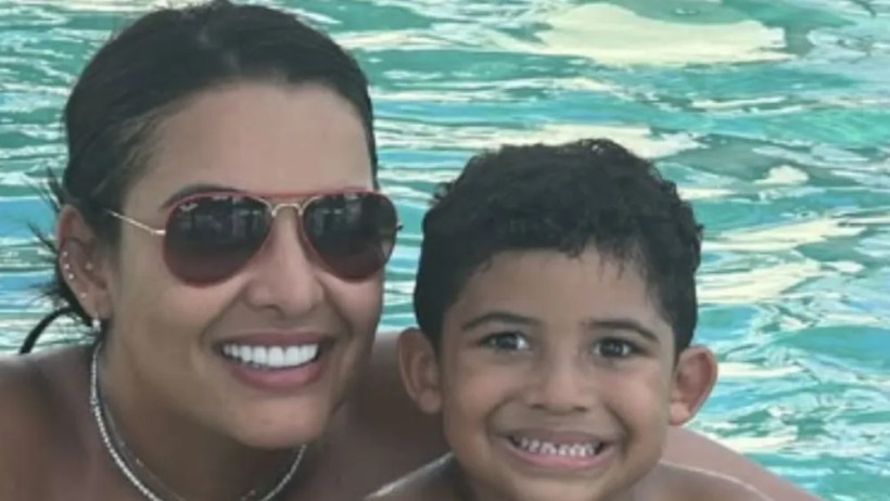 Mãe e filho sorrindo juntos em uma piscina clara.