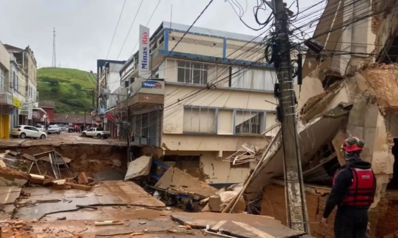 Cena de deslizamento de terra em área urbana, com construção danificada e um homem observando os destroços.