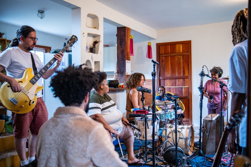 Grupo musical ensaiando em um ambiente aconchegante, com diversos instrumentos, como guitarra, bateria e microfones.