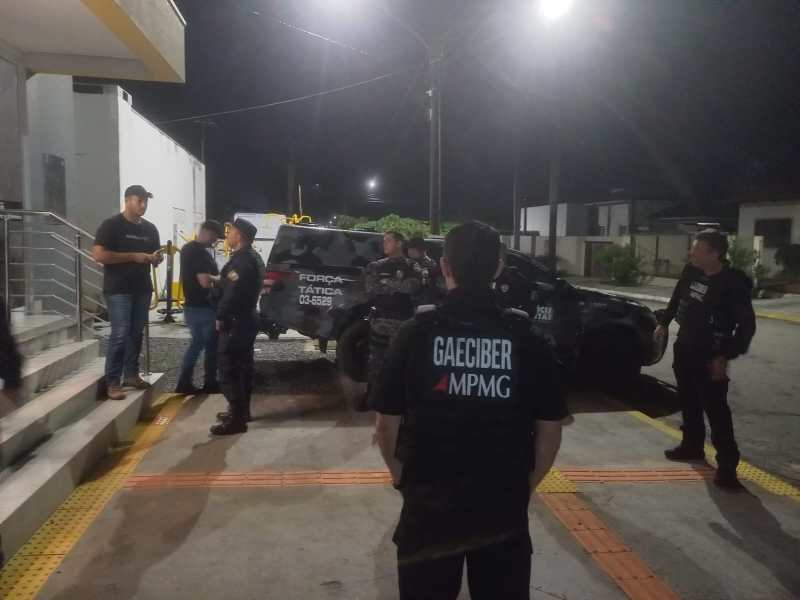 Grupo de policiais conversando em frente a um veículo da Força Tática à noite, com iluminação artificial ao fundo.