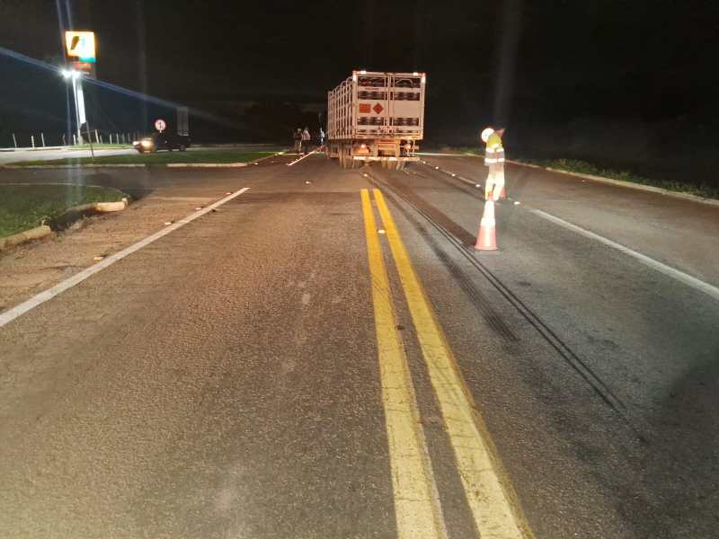 Estrada à noite com um caminhão parado, sinalização de trânsito e marcas de pneu visíveis no asfalto.