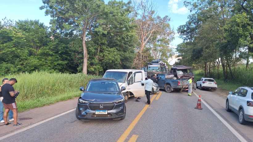 Acidente de carro em uma estrada com vários veículos envolvidos, incluindo vans e caminhões, e pessoas ao redor avaliando a situação.