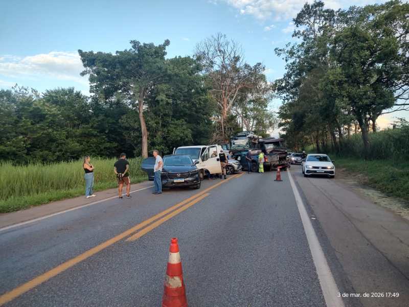 Acidente de trânsito na estrada com vários veículos envolvidos e pessoas conversando ao lado.