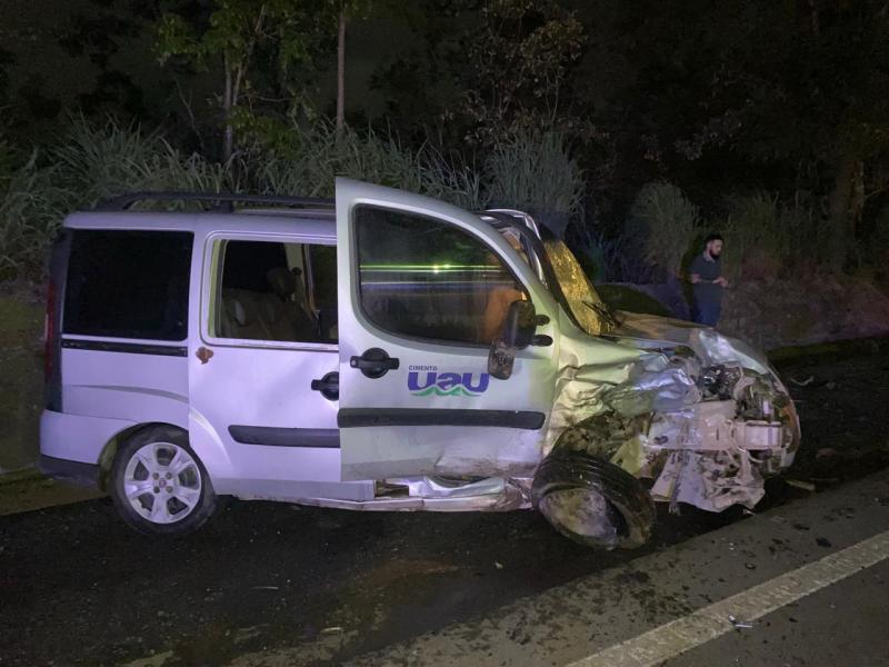Van branca acidentada na estrada, com parte frontal danificada e porta aberta, à noite.