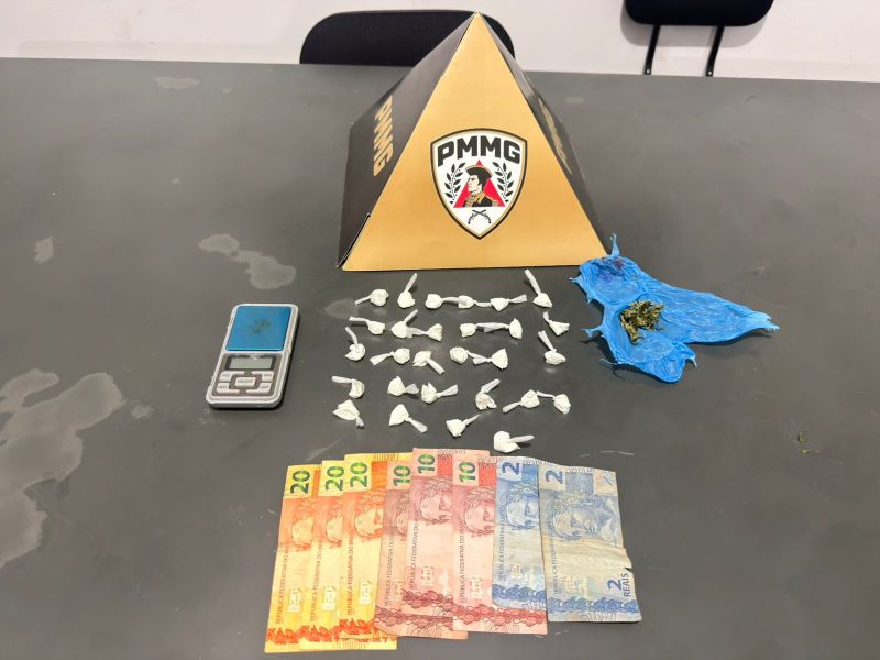 Material apreendido em uma operação policial, incluindo uma balança, pacotes de drogas e notas de dinheiro, sob uma pirâmide com o logo PMMG.