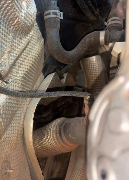 Visão de componentes de um motor, incluindo tubos e materiais de isolamento, capturada debaixo do veículo.