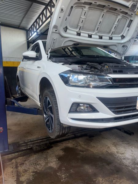 Carro branco em uma oficina com o capô levantado, localizado em uma plataforma de elevação.