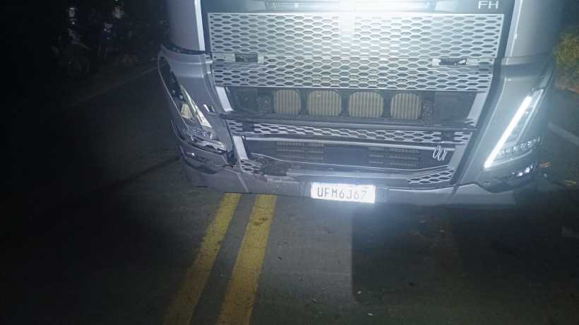 Caminhão com a parte da frente danificada parado em uma estrada à noite.