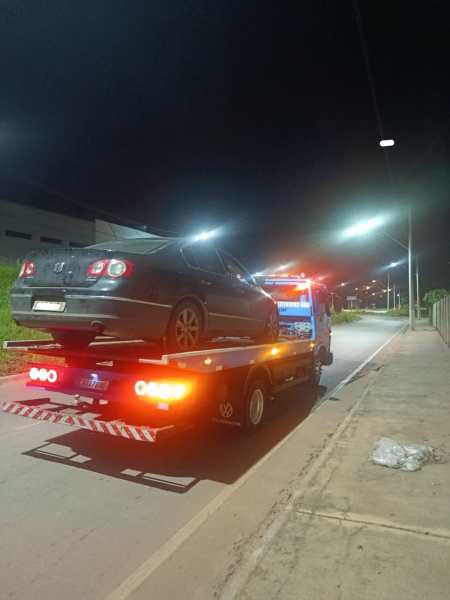 Caminhão guincho removendo um carro preto à noite em uma rua iluminada.