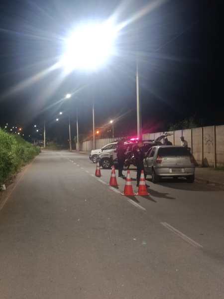 Cenas noturnas de uma rua com cones de sinalização e policiais em ação, observando veículos sob luzes brilhantes.