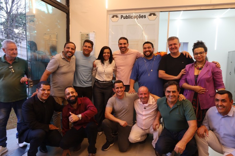 Grupo de pessoas sorrindo para a câmera em ambiente interno, com uma placa de 'Publicações' ao fundo.