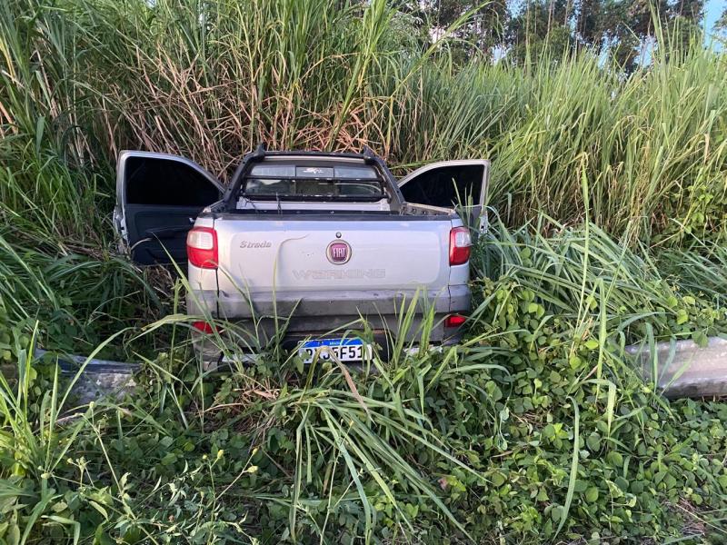 Foto de uma caminhonete Fiat Strada encostada em uma área com grama alta e densa, com as portas abertas.