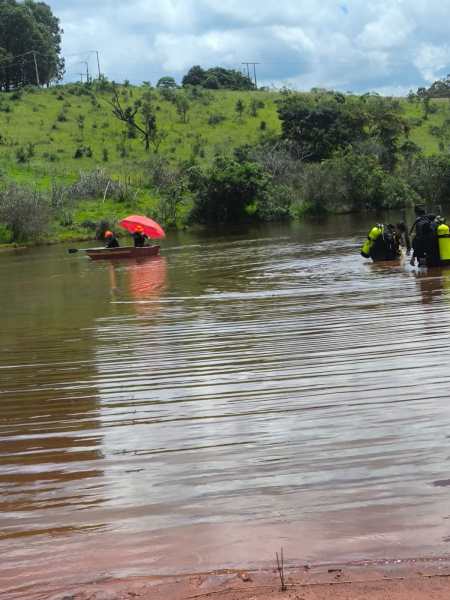Pessoas em um rio, com um homem em um barco sob um guarda-chuva vermelho e mergulhadores na água.