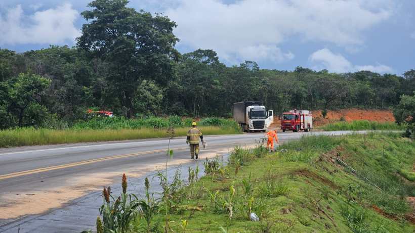 Caminhão parado na beira da estrada com bombeiros e trabalhadores, cercado por vegetação.