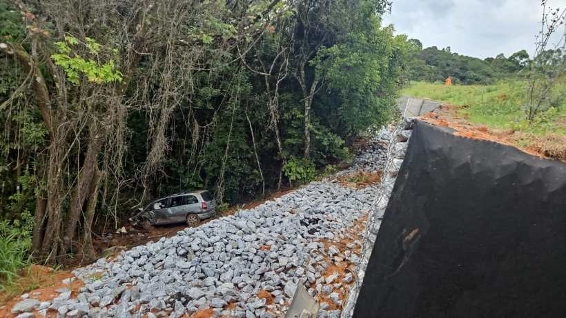 Carro encostado em um terreno coberto por pedras, próximo a uma área florestal.