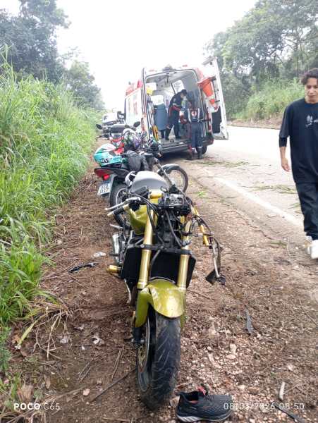 Acidente de moto na estrada, com ambulância ao fundo e motociclistas parados ao lado.