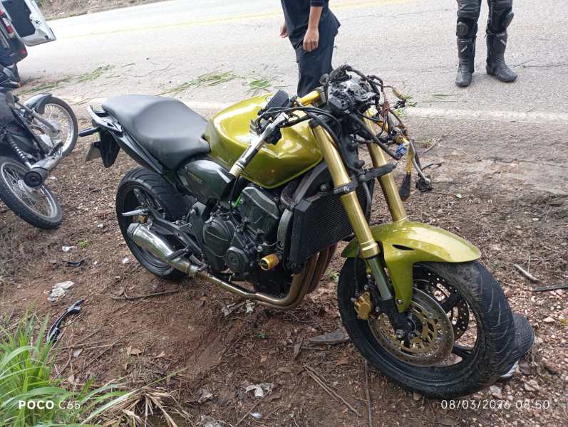 Motocicleta verde danificada ao lado da estrada, com pneus murchos e peças expostas.
