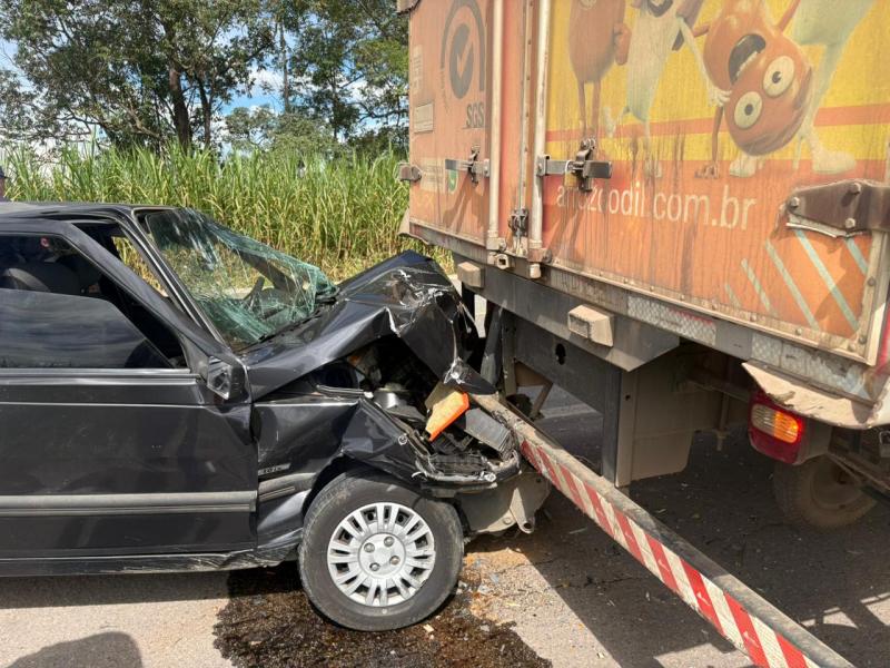 Acidente de carro envolvendo um veículo preto colidido na traseira de um caminhão parado na estrada.