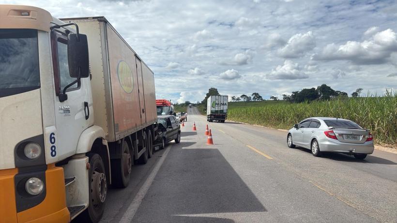 Caminhões e um carro parados em uma estrada com cones de sinalização, ao lado de um campo de cana-de-açúcar sob céu nublado.