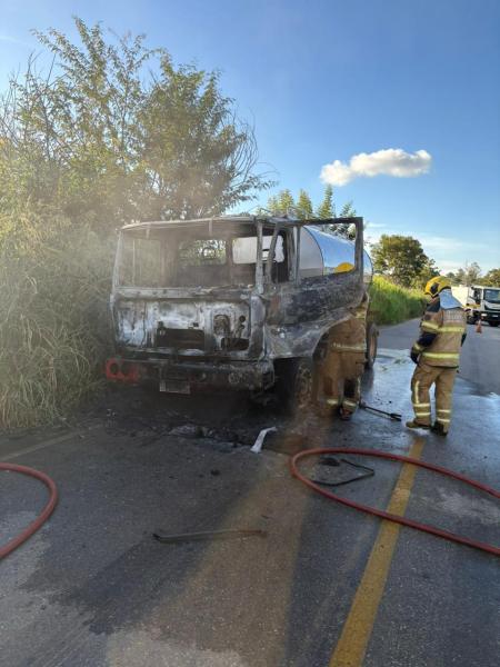 Caminhão queimado ao lado da estrada, com bombeiros realizando os cuidados necessários.