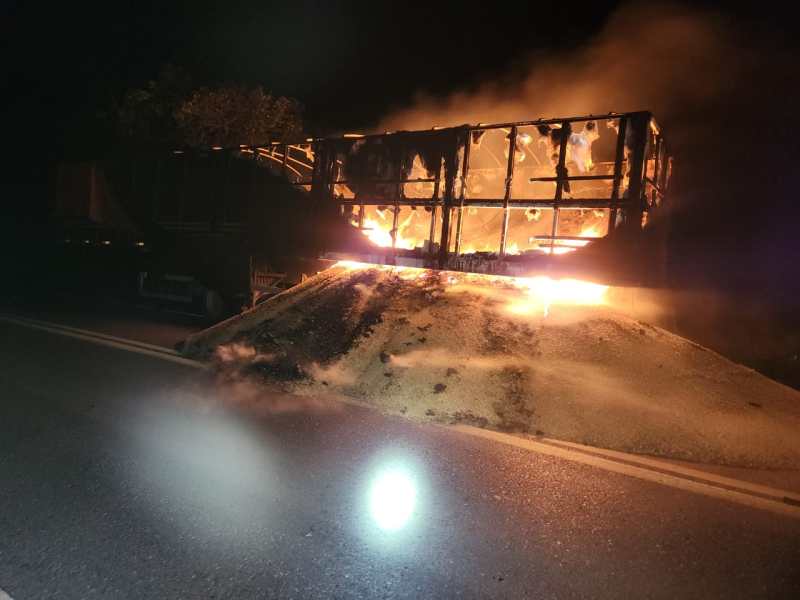 Caminhão pegando fogo à noite, com fumaça e chamas visíveis em sua carga.