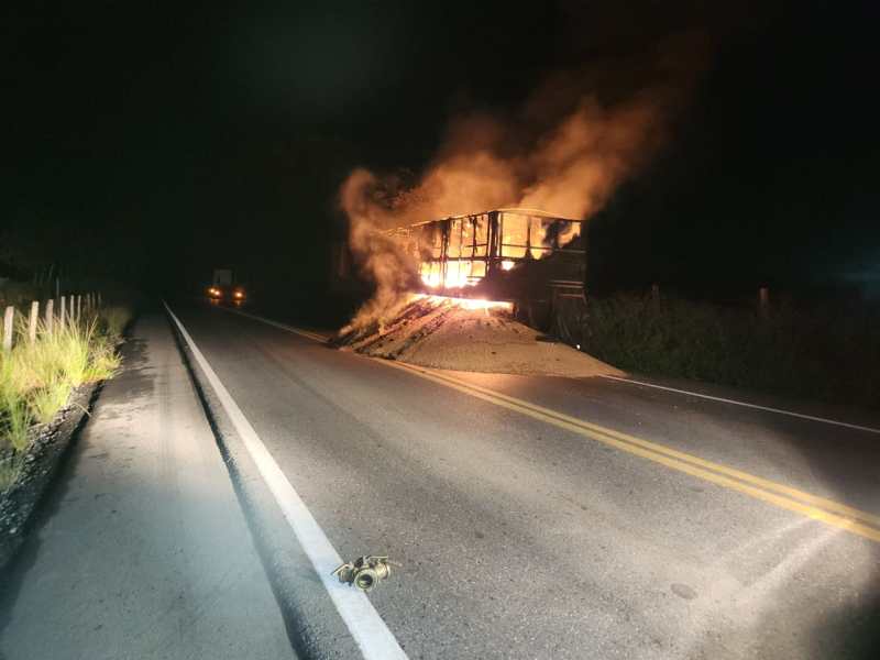 Um caminhão em chamas à noite, fumos subindo enquanto arde em uma estrada deserta.