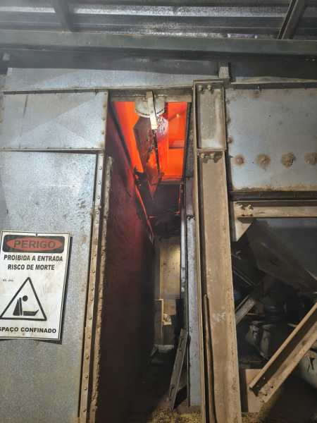 Visão de um espaço confinado com iluminação laranja, mostrando uma passagem estreita e um aviso de perigo na parede.