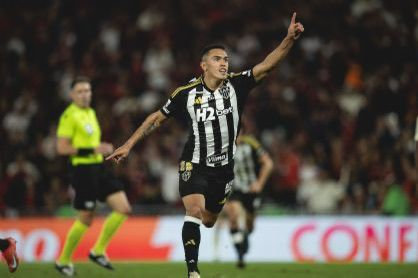 A soccer player celebrating after scoring a goal, wearing a black and white striped jersey.