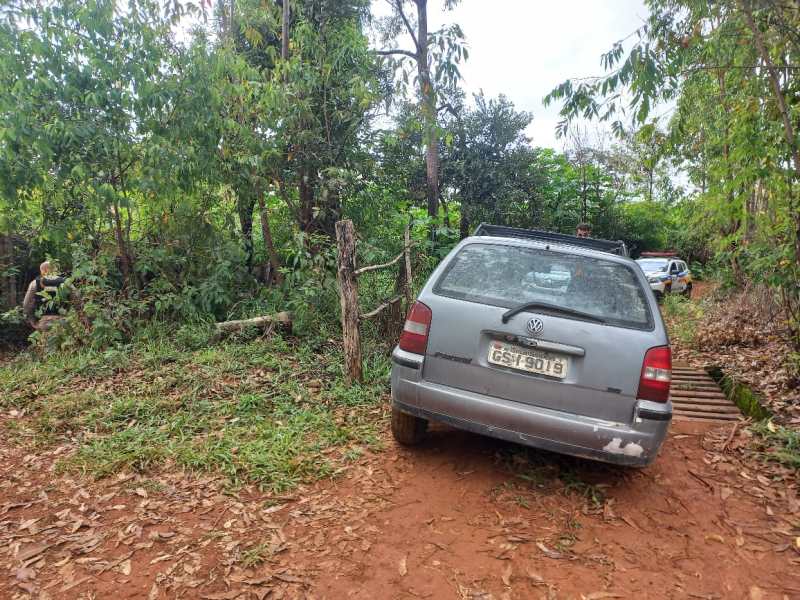 Carro estacionado em uma estrada de terra, cercado por árvores e vegetação.