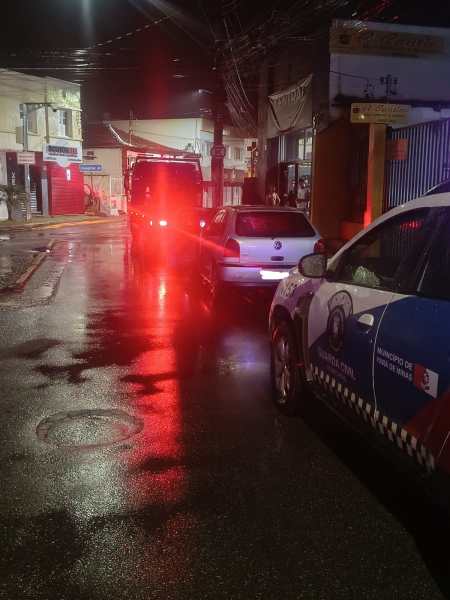Um carro da polícia parando em uma rua à noite, com luzes vermelhas refletindo no pavimento molhado.