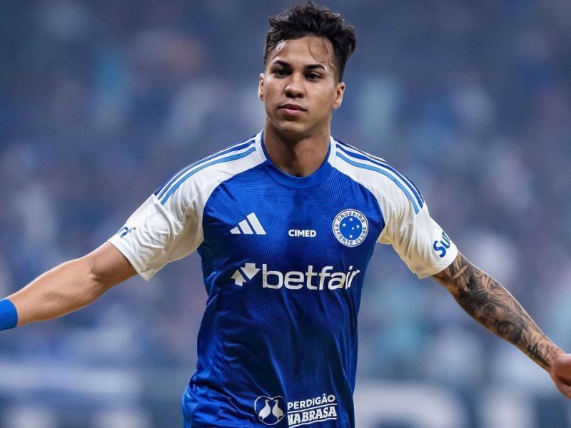 A football player celebrating a goal, wearing a blue team jersey with white sleeves and sponsor logos.