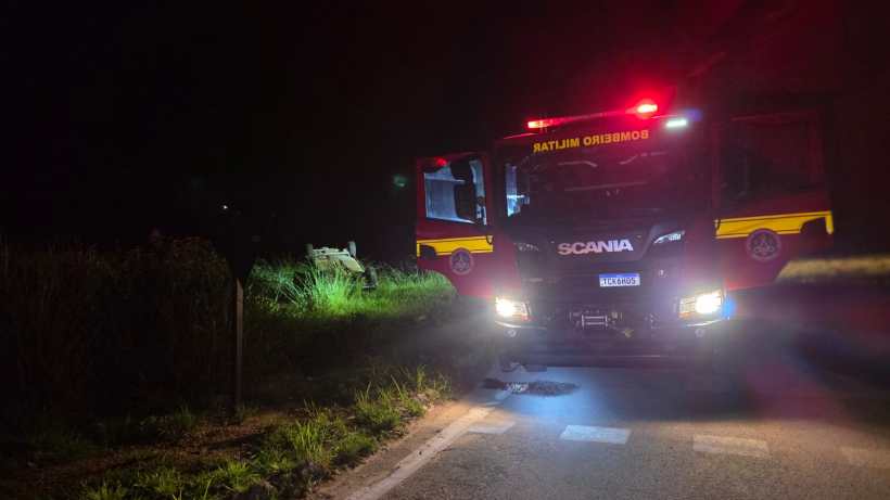Caminhão de bombeiros estacionado à noite em uma estrada com luzes de emergência acesas.