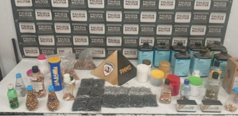 Mesa com diversas embalagens de substâncias, frascos e cápsulas, em frente a um fundo com logos da Polícia Militar.