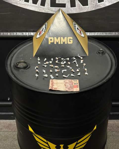 Um barril preto com um cúpula dourada contendo o texto "PMMG" no topo. Em cima do barril há várias pequenas amostras dispostas em forma de letras e uma nota de 10 reais.