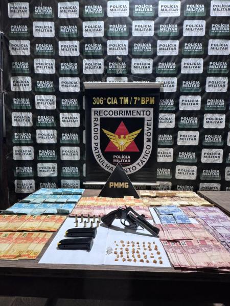 Imagem de uma mesa com dinheiro, drogas e armas, com um banner da polícia militar ao fundo.