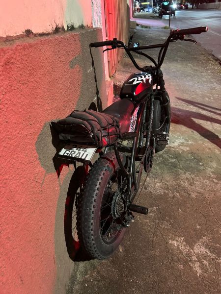 Uma bicicleta estacionada encostada em um muro, com um design robusto e pneus grandes, durante a noite.