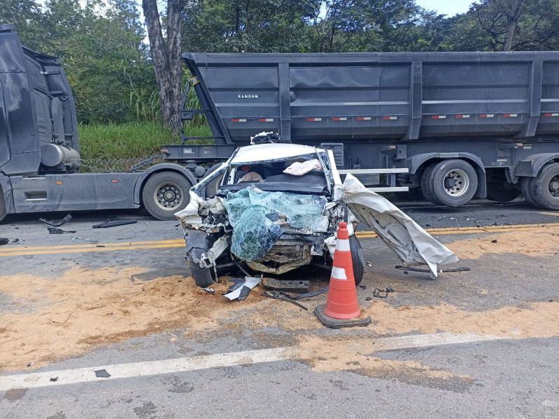 Imagem de um carro destruído em um acidente de trânsito ao lado de um caminhão, com vidro quebrado e sinais decolisão, sinalização de trânsito e detritos na estrada.