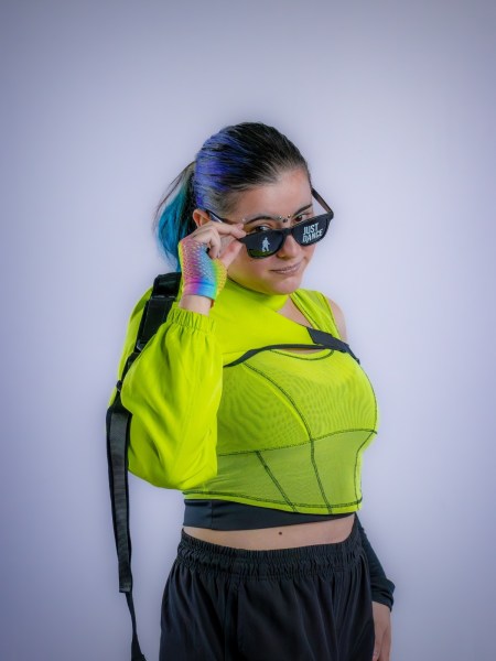 Modelo usando blusa transparente verde limão e óculos escuros, com cabelo preso e destaque em tonalidades de azul.
