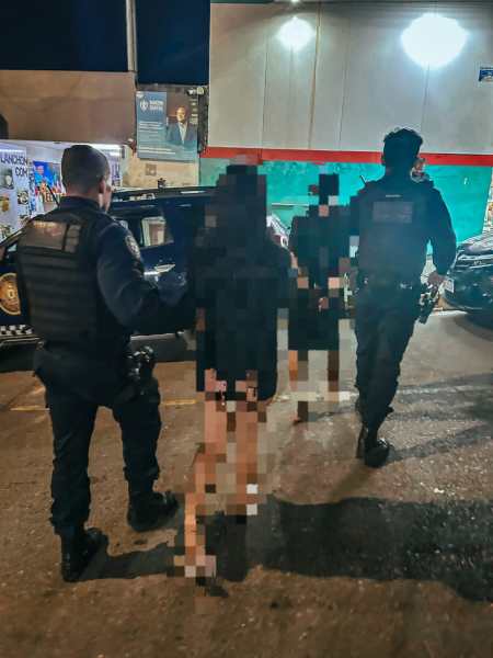 Policiais acompanhando duas pessoas em um ambiente urbano à noite.
