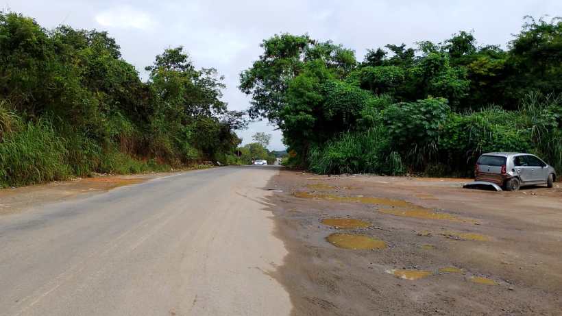 Uma estrada de terra com vegetação ao redor e um carro estacionado à direita.