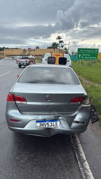Carro acidentado na estrada, com danos na parte traseira e placas indicativas de direção.