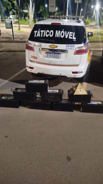 Veículo da polícia com a inscrição 'TÁTICO MÓVEL' estacionado, com várias caixas pretas dispostas em linha à frente.